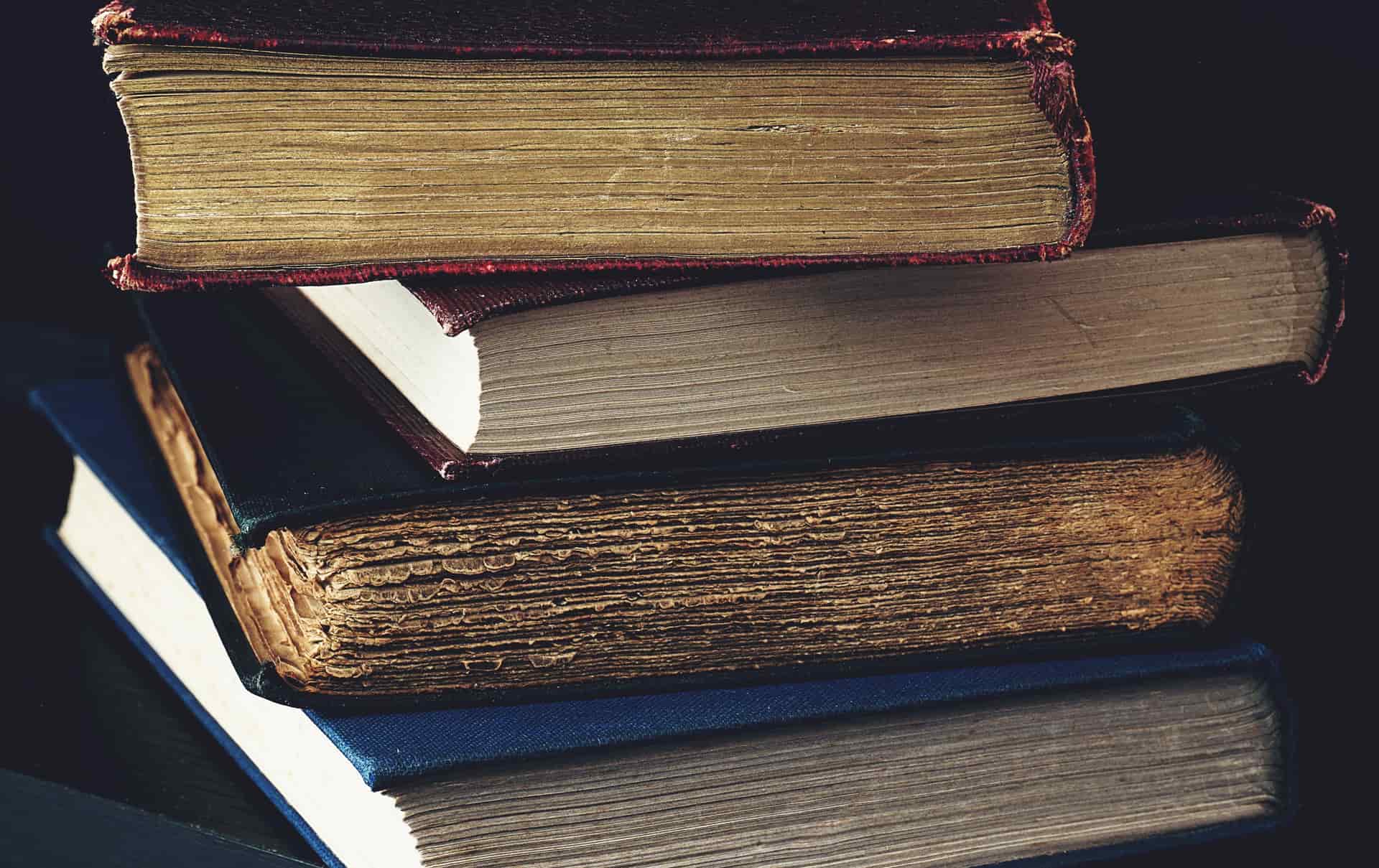 A stack of old hardcover books lit by candlelight