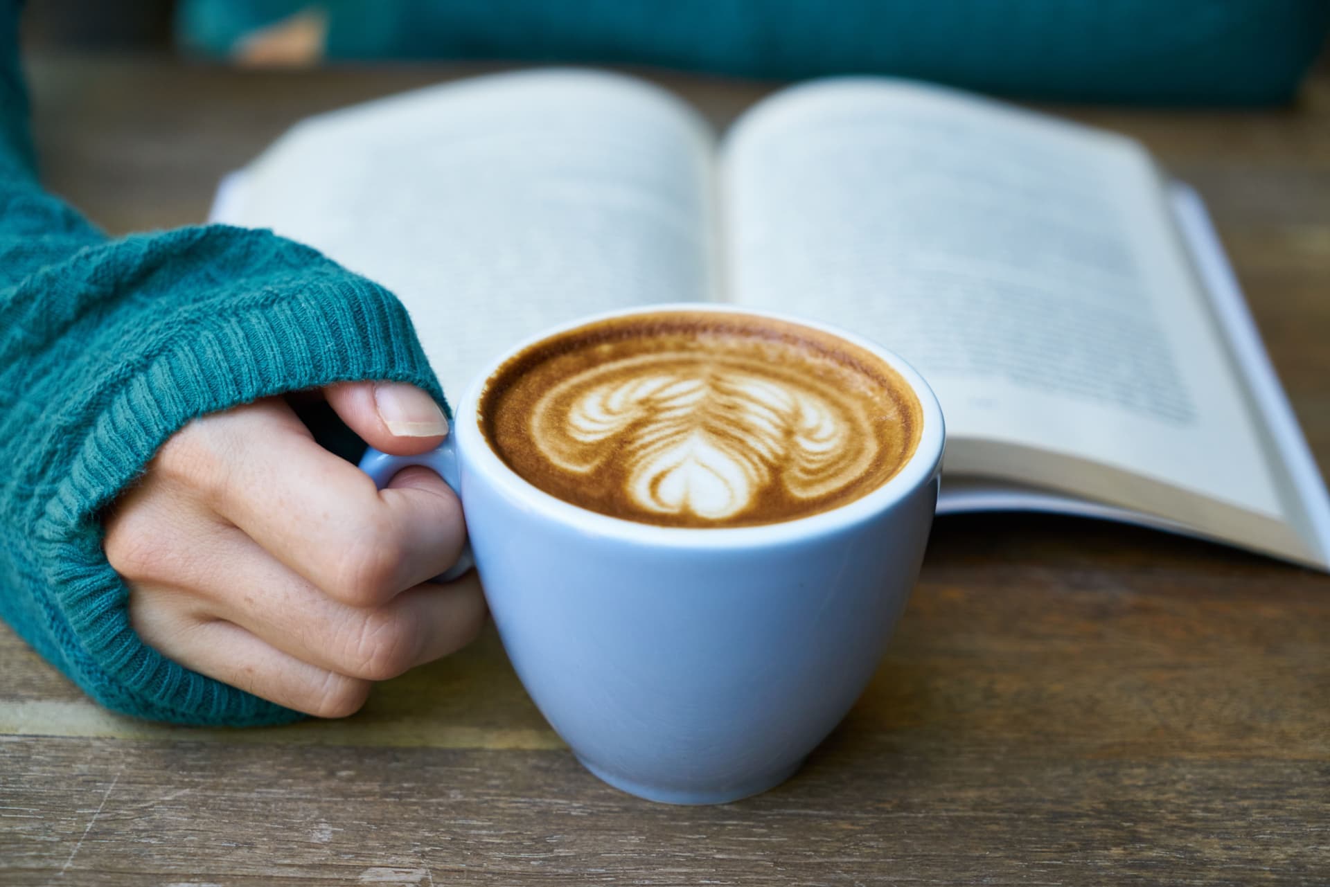 Hands holding an open book beside a mug of coffee
