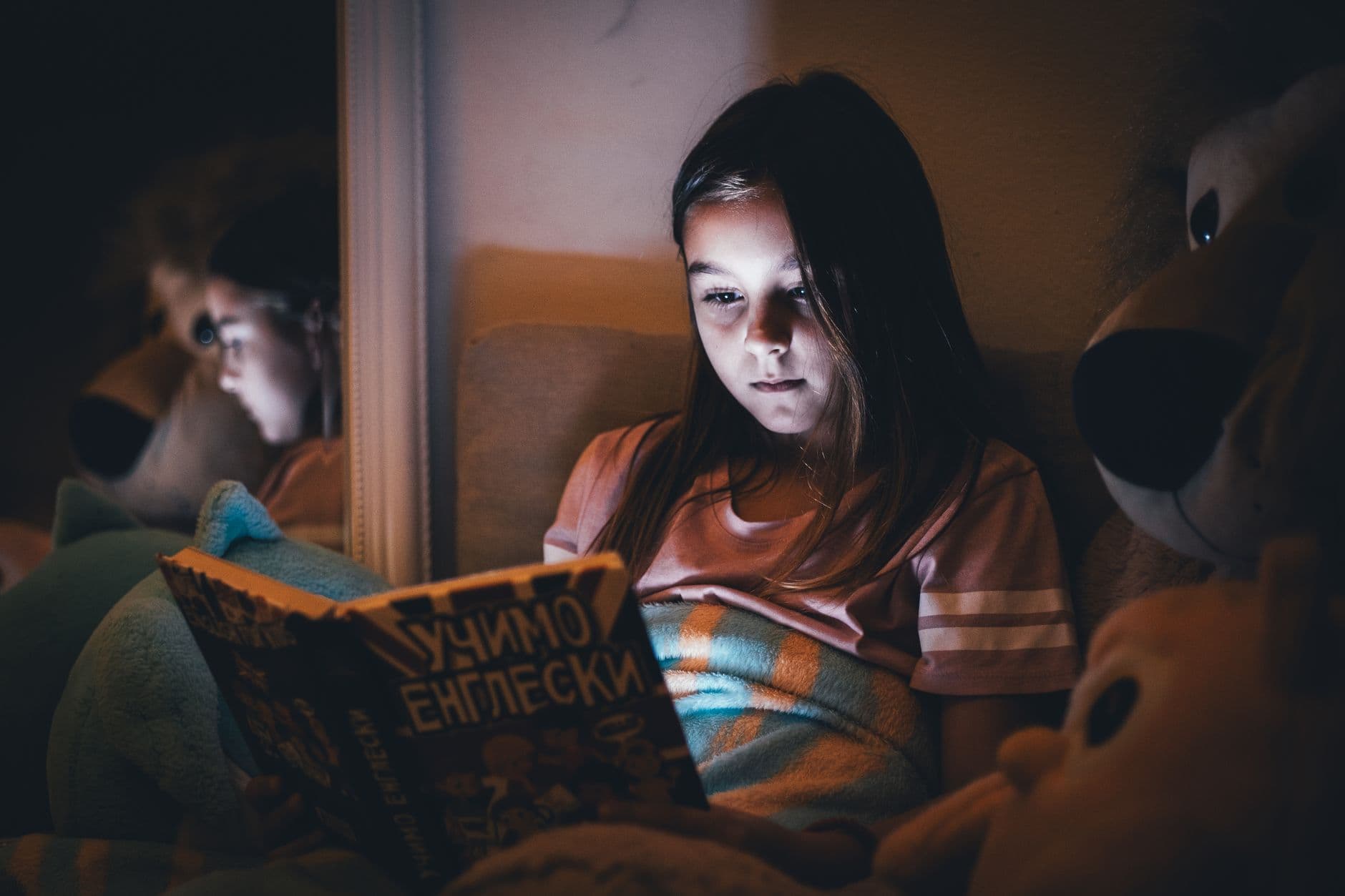 A girl reading a book by the light of a small lamp
