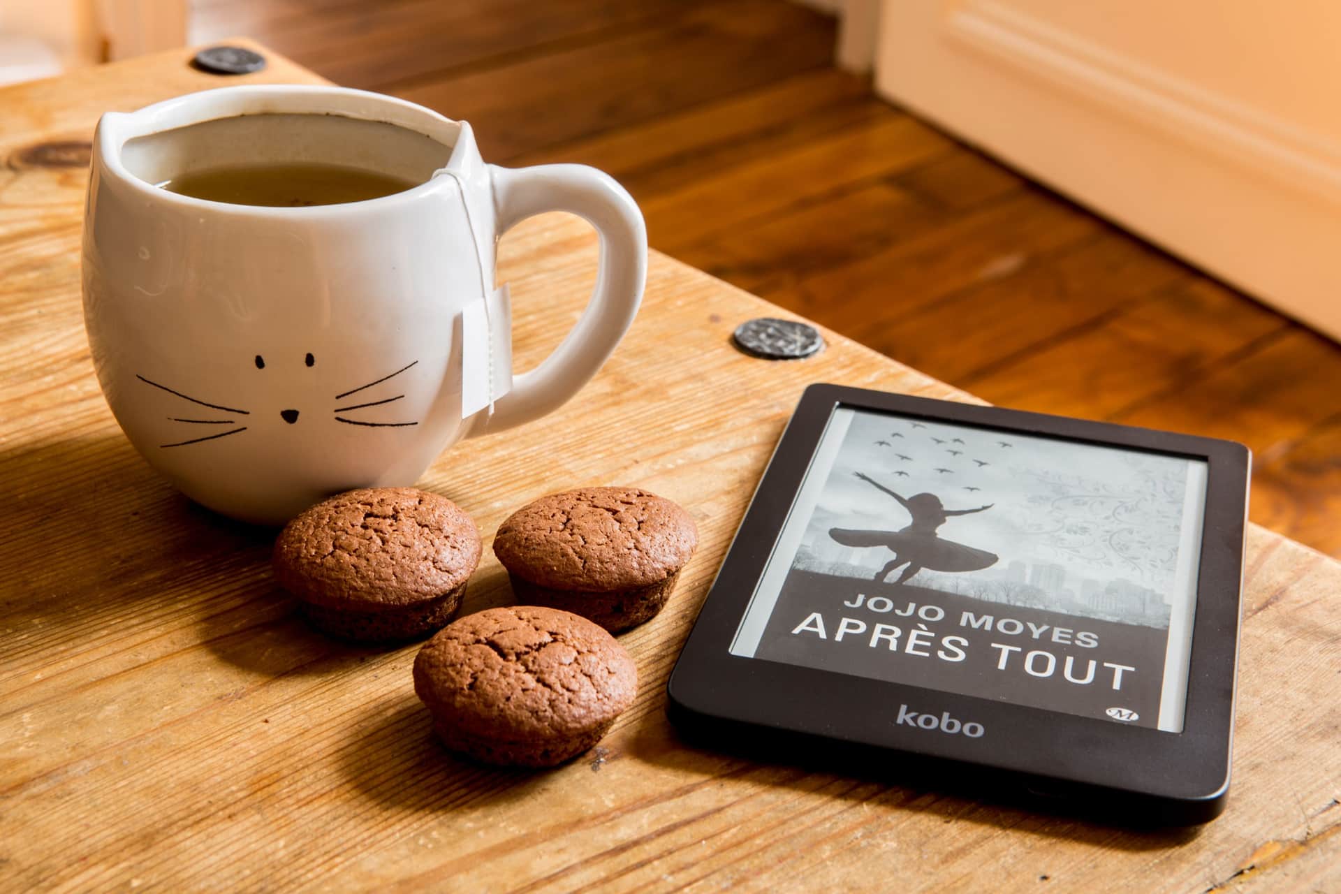 An e-reader lying on a wooden table beside a cup of coffee
