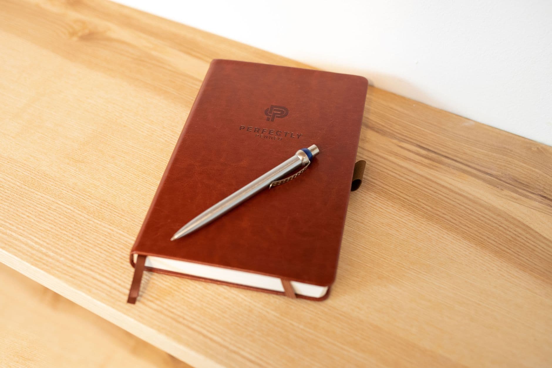 A leather-bound notebook and pen resting on a wooden desk