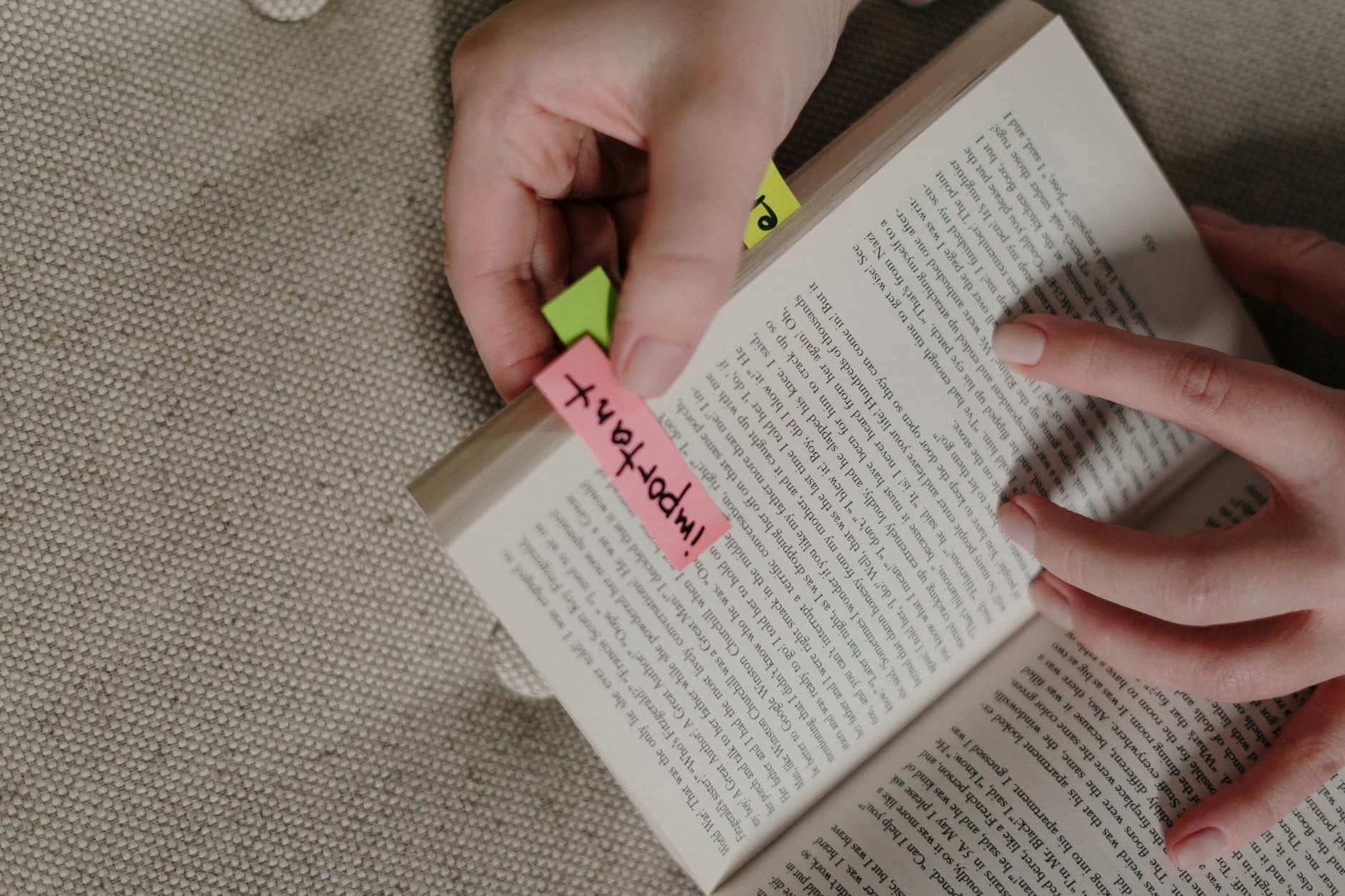A teenager reading a book on a bed beside a stack of paperbacks