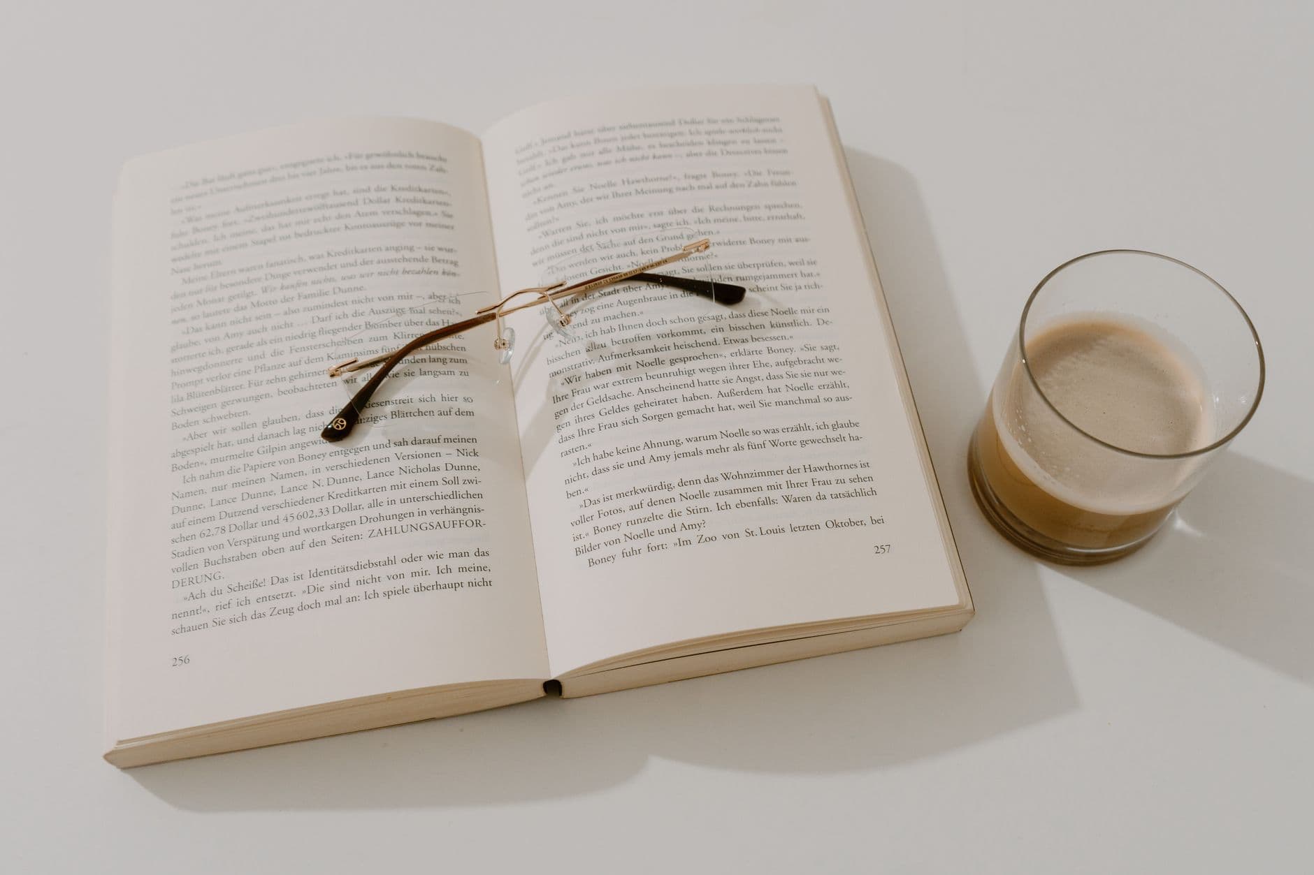 An open book lying flat on a table beside reading glasses and a coffee