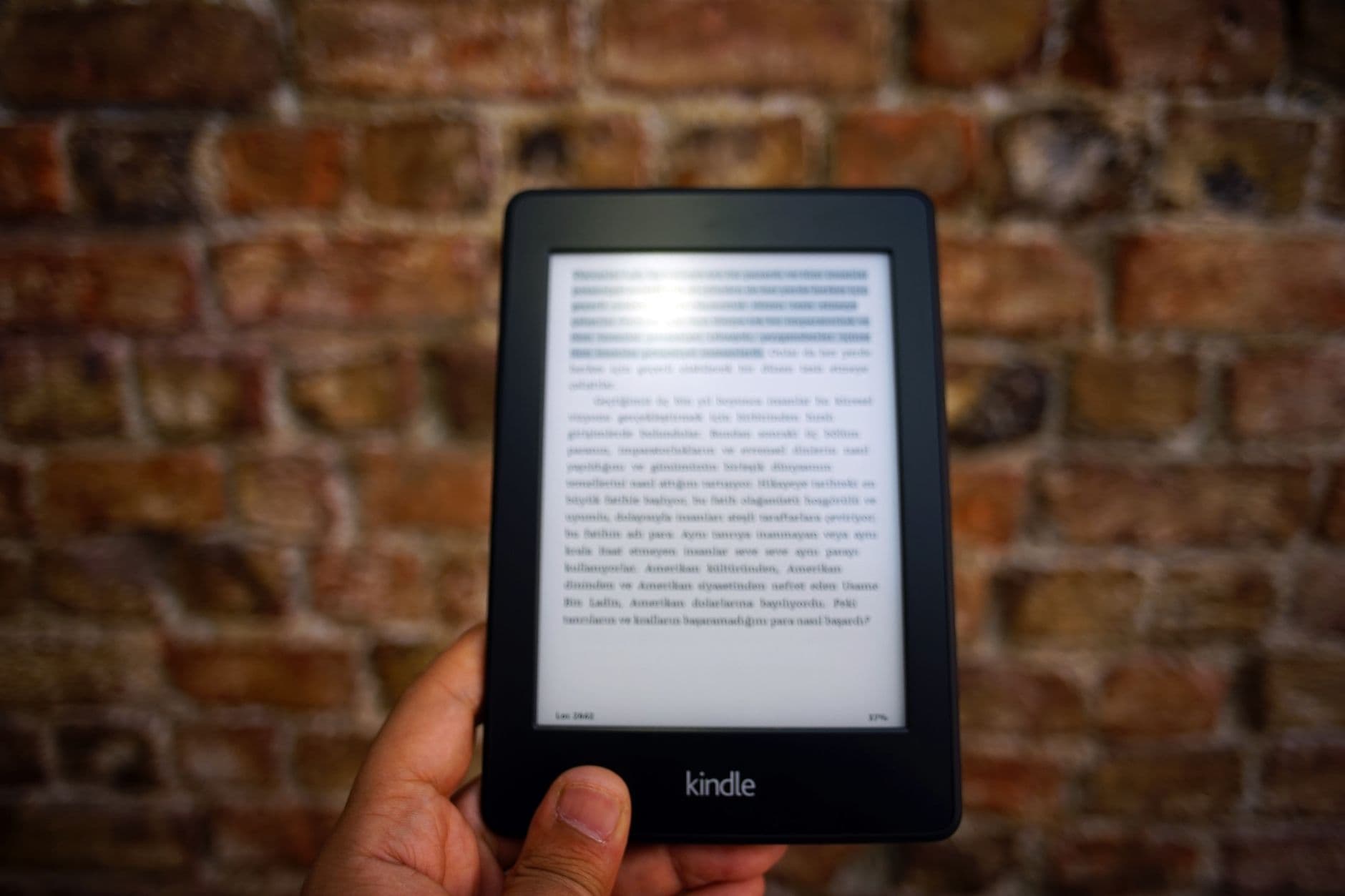 A hand holding a Kindle e-reader against a brick wall