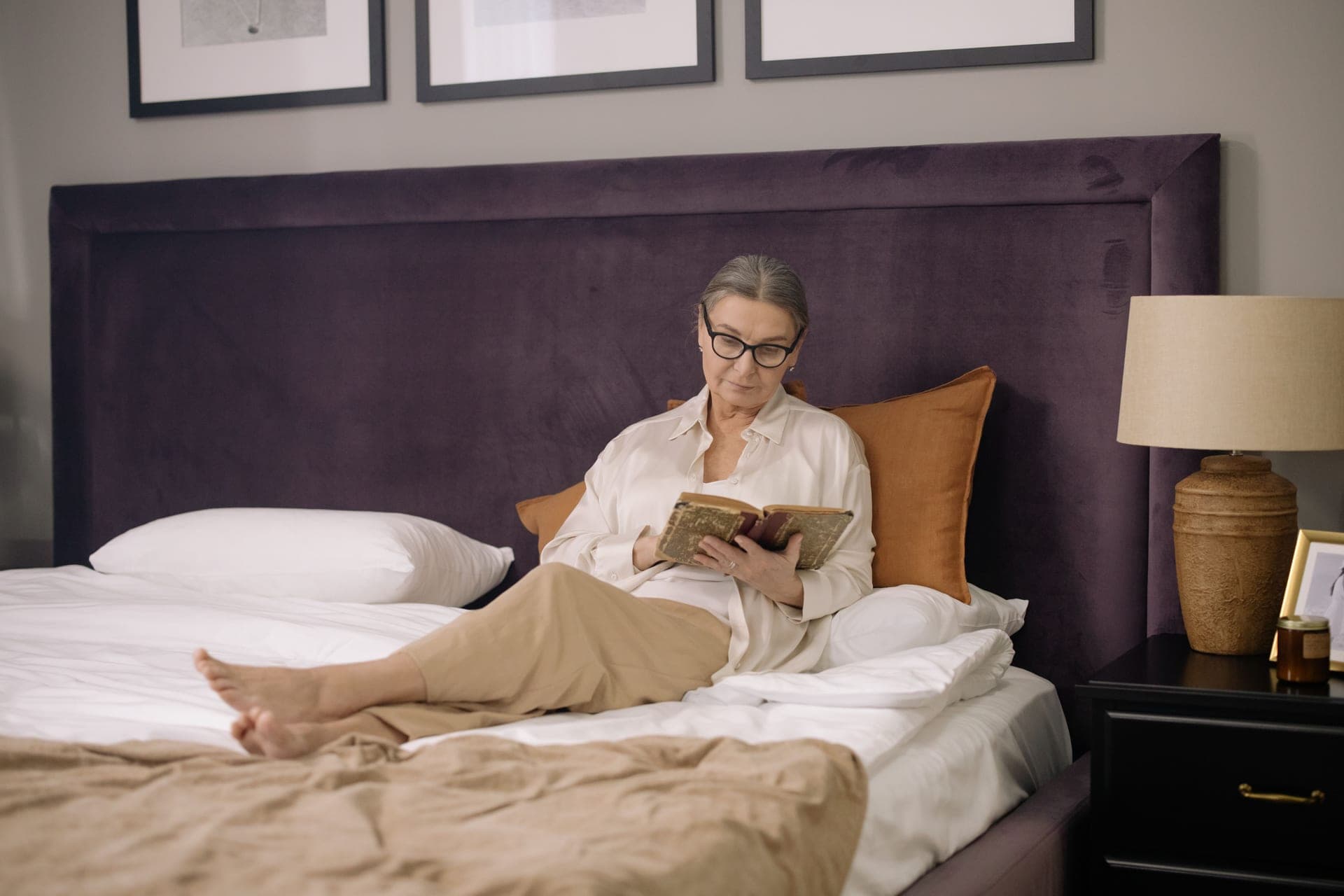 A person reading a book in bed at night by the light of a small lamp