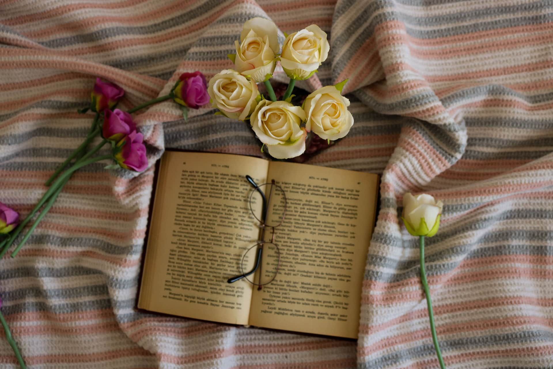A book lying open on a bed beside pink flowers
