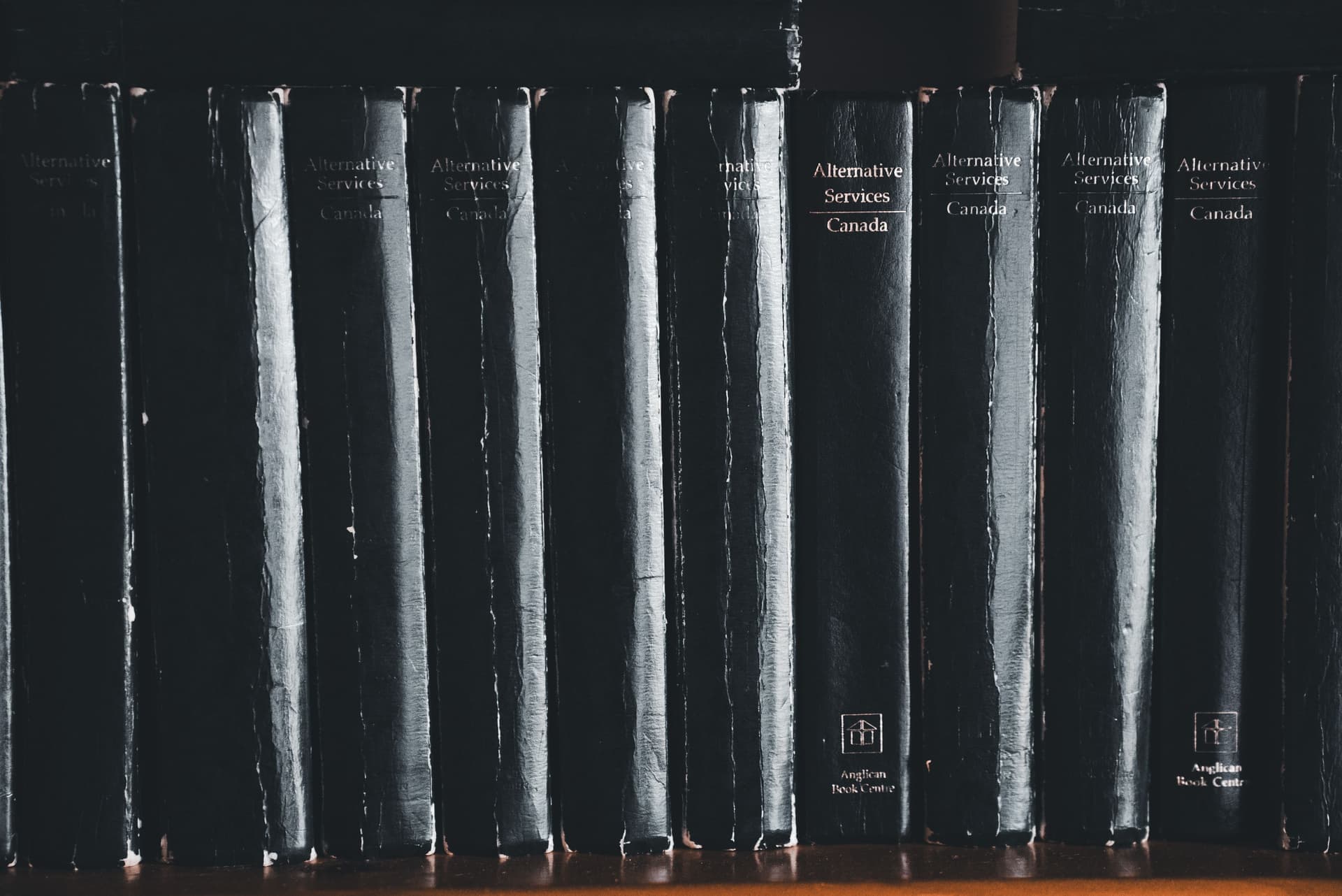A row of books leaning to one side on a wooden shelf